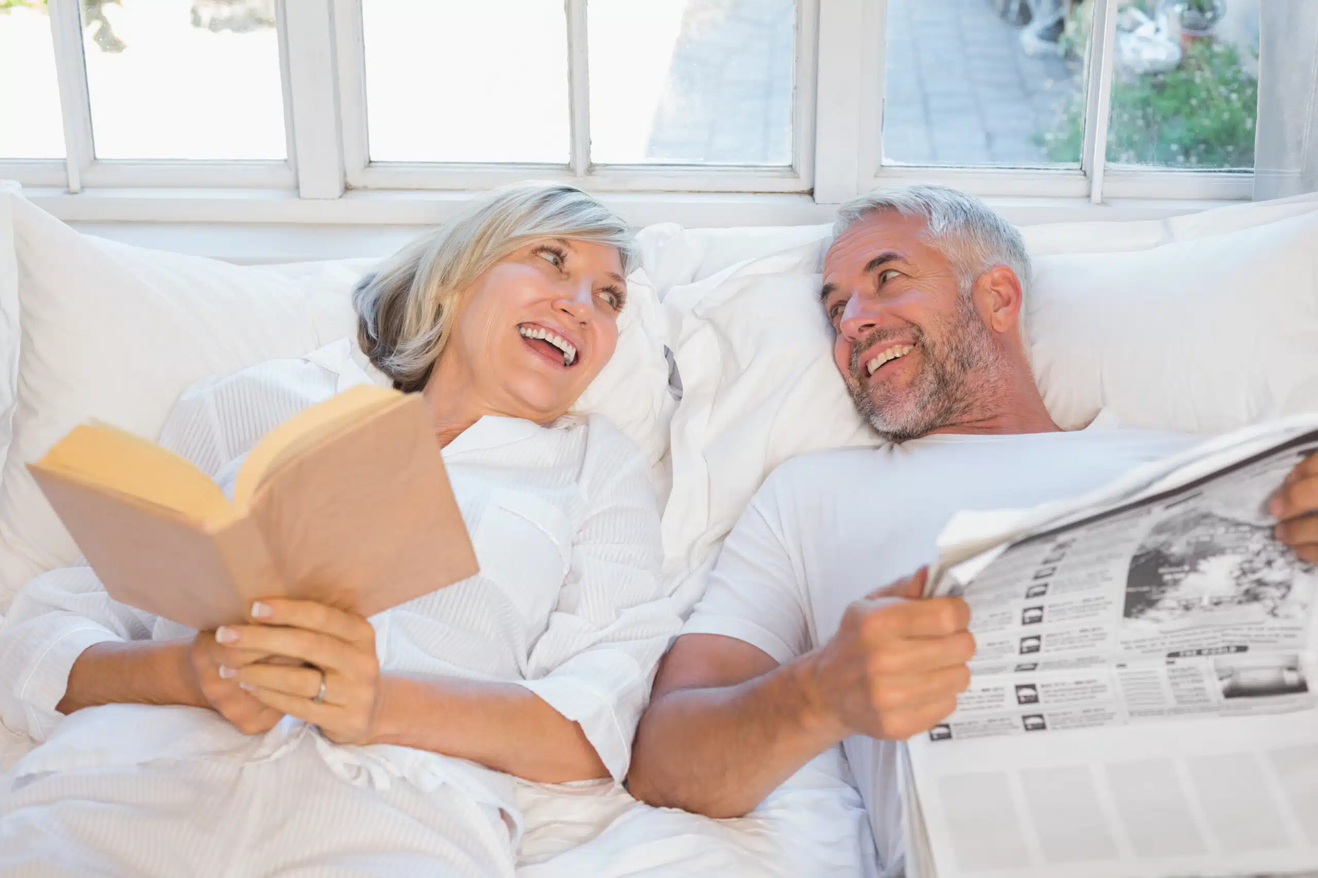 cheerful mature couple with newspaper book bed scaled